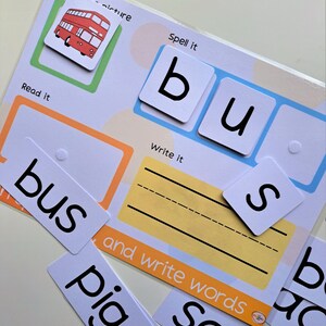 May include: A red double-decker bus illustration with the word "bus" written below it.  The word "bus" is also spelled out with individual letter tiles.  The words "Spell it", "Read it", and "Write it" are printed on the page.  There are also blank lines for writing the word "bus".
