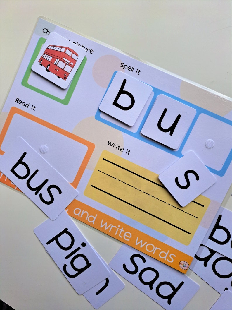 May include: A red double-decker bus illustration with the word "bus" written below it.  The word "bus" is also spelled out with individual letter tiles.  The words "Spell it", "Read it", and "Write it" are printed on the page.  There are also blank lines for writing the word "bus".