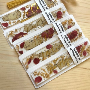 Pode incluir: Conjunto de seis marcadores de p&aacute;gina feitos &agrave; m&atilde;o com folha de ouro e p&eacute;talas de rosa secas embutidas em resina transparente. Cada marcador de p&aacute;gina apresenta um fundo de papel de estilo vintage com texto de caligrafia dourada. O texto nos marcadores de p&aacute;gina diz "The Calm", "The Domin", "The Gr", "The Holl", "The Follow", e "The Co".