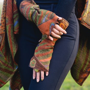 May include: Fingerless gloves featuring a multi-colored abstract pattern in shades of olive green, burnt orange, and deep purple. The gloves are crafted from a textured fabric and include a small wooden toggle button closure and a floral detail.