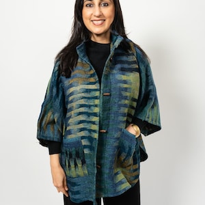 Puede incluir: Una chaqueta estampada en azul, verde y marrón con botones de madera y bolsillos. La chaqueta tiene un corte holgado con mangas tres cuartos. La persona lleva un top negro y pantalones negros.
