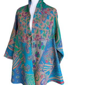 May include: A long-sleeved jacket featuring a vibrant patchwork design with various patterns in shades of teal, blue, green, orange, and tan. The garment has a single large wooden button closure at the center front and a wide, open collar neckline.