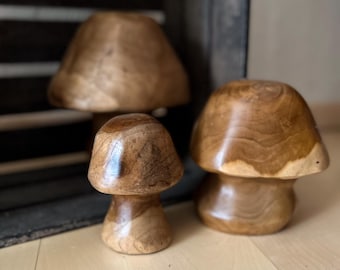 Op de afbeelding: Drie gesneden houten paddenstoelsculpturen van verschillende groottes, elk met een gladde, gepolijste afwerking die de natuurlijke houtnerfpatronen en texturen van het bruine hout benadrukt. De paddenstoelen hebben ronde hoeden en stelen.