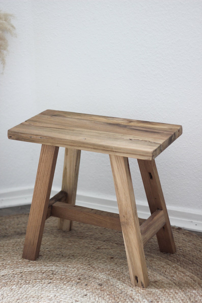 May include: A rustic wooden stool with a natural wood finish. The stool has a simple design with four legs and a rectangular seat.
