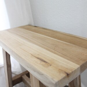 May include: A light wood bench with a simple design and a natural finish. The bench has a wide, flat top and sturdy legs.