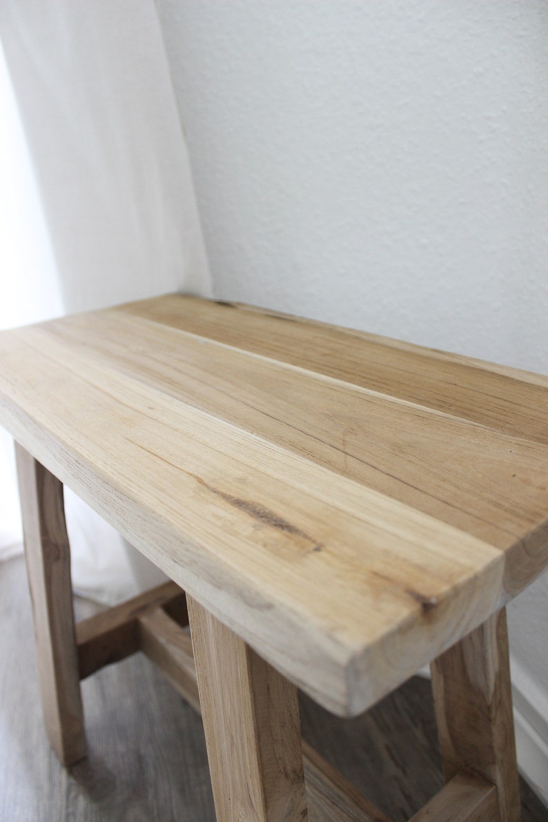 May include: A light wood bench with a simple design and a natural finish. The bench has a wide, flat top and sturdy legs.