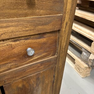 K&ouml;nnte beinhalten: Nahaufnahme eines Holzschranks mit zwei Schubladen und einer Schrankt&uuml;r. Der Schrank besteht aus einem warm get&ouml;nten Holz mit sichtbarer Maserung und Metallkn&ouml;pfen. Der Schrank ist wahrscheinlich Teil einer gr&ouml;&szlig;eren M&ouml;belserie.