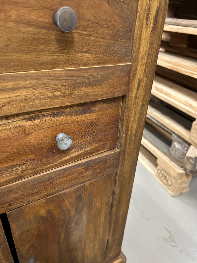 K&ouml;nnte beinhalten: Nahaufnahme eines Holzschranks mit zwei Schubladen und einer Schrankt&uuml;r. Der Schrank besteht aus einem warm get&ouml;nten Holz mit sichtbarer Maserung und Metallkn&ouml;pfen. Der Schrank ist wahrscheinlich Teil einer gr&ouml;&szlig;eren M&ouml;belserie.