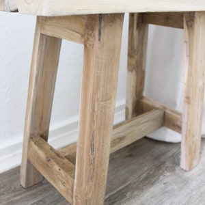 May include: A light wood bench with a simple design. The bench has a rectangular top and four legs. The legs are connected by a horizontal support beam.