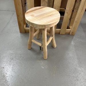 Pode incluir: Um pequeno banco redondo de madeira com acabamento natural. O banco tem um assento circular e três pernas resistentes. As pernas são conectadas ao assento com um design simples e rústico. O banco é feito de madeira clara e é adequado.