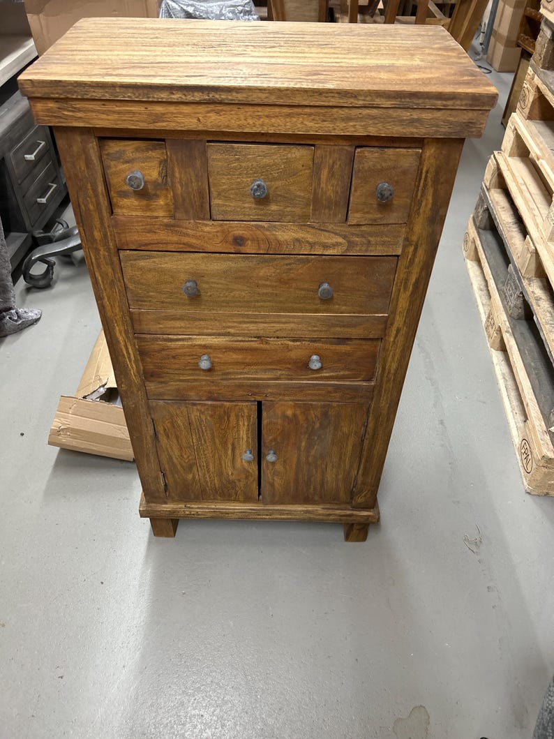 K&ouml;nnte beinhalten: Ein Holzschrank mit warmbraunem Finish. Er verf&uuml;gt &uuml;ber mehrere Schubladen und einen zweit&uuml;rigen Schrank am unteren Ende. Der Schrank hat eine rechteckige Form und wird wahrscheinlich zur Aufbewahrung verwendet. Die Beschl&auml;ge sind aus dunklem Metall.