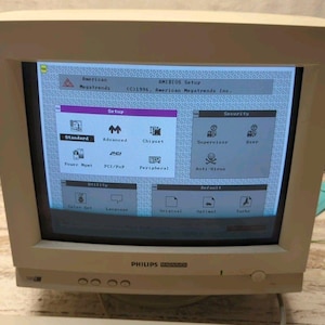 May include: A beige Philips computer monitor showing the AMIBIOS setup screen. The display features setup options like Standard, Advanced, and Security. The monitor has a power button and control buttons on the front, typical of older computer hardware.