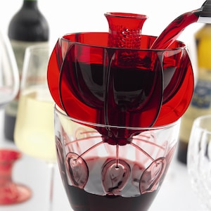 May include: A red wine aerator with a clear glass wine glass underneath. Red wine is being poured into the aerator from a bottle.