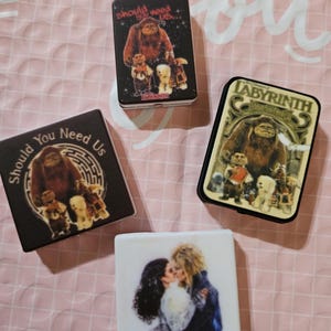 May include: Four small, rectangular boxes with images from the movie Labyrinth. One box features a kissing couple, while the others display characters and text like "Should You Need Us" and "Labyrinth". The boxes are black and white with colorful images.