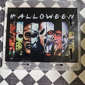 May include: A rectangular, clear plastic license plate featuring the word "HALLOWEEN" in white, stylized like the TV show "Friends." The plate showcases a collage of horror movie villains, including Jason Voorhees and Pennywise.