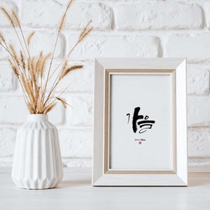 Puede incluir: Una impresión enmarcada en blanco con caligrafía negra que dice "Otoño" en japonés. La impresión está en una pared de ladrillo blanco con un jarrón de hierba seca en primer plano.