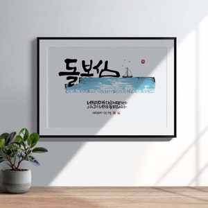 Könnte beinhalten: Ein gerahmter Druck mit einem blauen und weißen Aquarellhintergrund, der ein Segelboot auf dem Wasser zeigt. Der Druck zeigt koreanische Kalligraphie in schwarzer Tinte, die "돌보심" lautet, was mit "Sorge tragen" oder "sich kümmern" übersetzt wird. Der Text unter der Kalligraphie lautet "CAST AWAY YOUR ANXIETY BECAUSE HE CARES FOR YOU" auf Englisch. Der Druck enthält auch koreanischen Text, der "너희를 돌보심이라" lautet, was mit "Er sorgt für dich" übersetzt wird.
