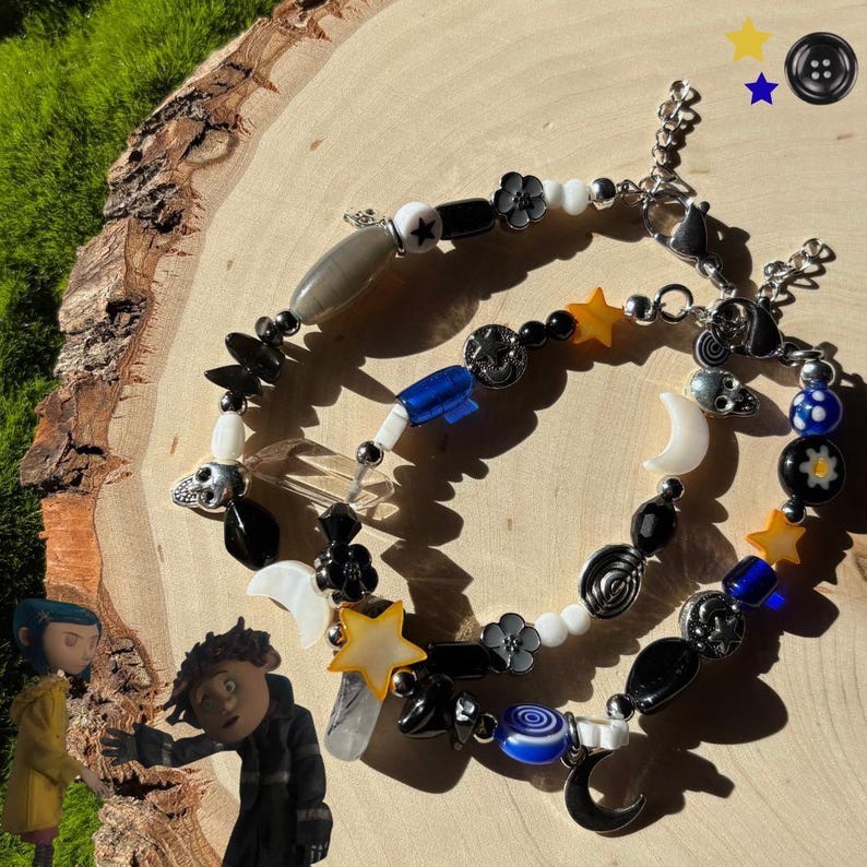 K&ouml;nnte beinhalten: Zwei Armb&auml;nder mit Perlen und verschiedenen Anh&auml;ngern, darunter Sterne, Monde, Blumen und Totenk&ouml;pfe. Die Armb&auml;nder haben schwarze, wei&szlig;e und blaue Perlen mit silberfarbenen Metallakzenten. Die Armb&auml;nder werden auf einer Holzoberfl&auml;che pr&auml;sentiert.