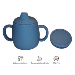 May include: A blue baby sippy cup with two handles and a lid. The lid is off to the side. The cup has the words "Lebensmittelecht", "Temperaturbest&auml;ndig", and "BPA Frei" with corresponding icons.