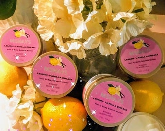 May include: Four jars of lemon-vanilla cream hair and body smooth butter, each with a yellow lemon and vanilla bean illustration on the label. The jars are arranged on a white surface with yellow lemons and white flowers.
