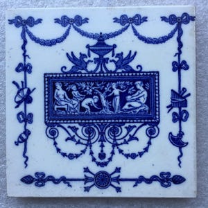 May include: Blue and white ceramic tile with a decorative design featuring a central scene of four figures in a garden setting. The tile is framed by a border of floral and geometric motifs.