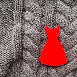 May include: A red paper dress cutout on a grey knitted fabric background.
