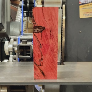 May include: A close-up of a red and black wood block with a unique grain pattern. The block is sitting on a metal surface.
