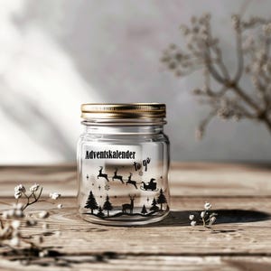 Könnte beinhalten: Ein klares Glas mit goldenem Deckel, verziert mit einer schwarzen Silhouette von Rentieren, die einen Schlitten ziehen, Bäumen und dem Text "Adventskalender to go". Geeignet für einen Adventskalender.
