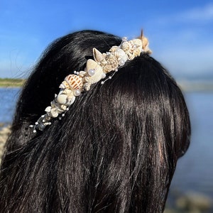 May include: A white seashell headband with pearls and small seashells. The headband is worn on a person with long black hair.