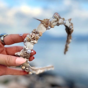 May include: A white headband decorated with seashells and pearls. The headband is a whimsical accessory for a beach-themed event.