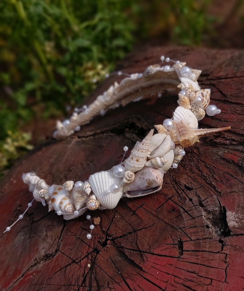 May include: A white headband decorated with seashells and pearls. The headband is made of a flexible material and is perfect for a beach wedding or a summer party.
