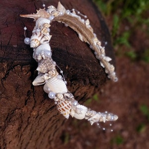 May include: A white and brown seashell crown with white pearl accents. The crown is made of natural seashells and is perfect for a beach wedding or a mermaid-themed party.