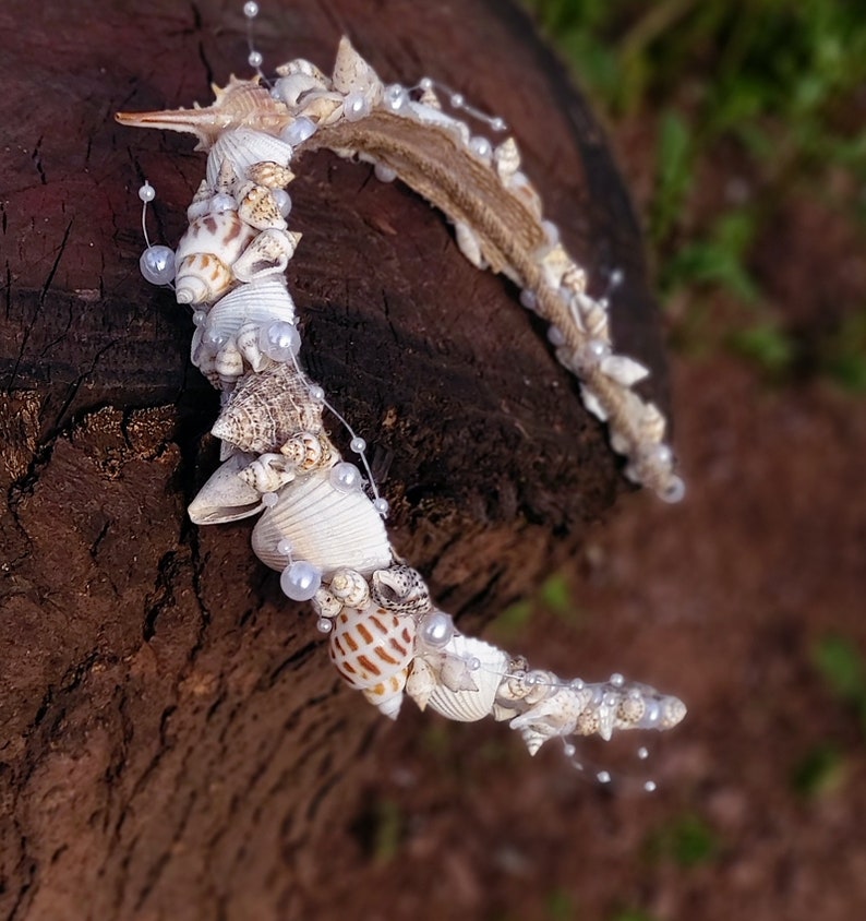 May include: A white and brown seashell crown with white pearl accents. The crown is made of natural seashells and is perfect for a beach wedding or a mermaid-themed party.