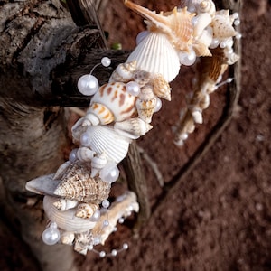 May include: A collection of seashells and pearls arranged in a decorative garland, wrapped around a tree branch. The seashells are various shapes and sizes, with some having a natural brown and white pattern.