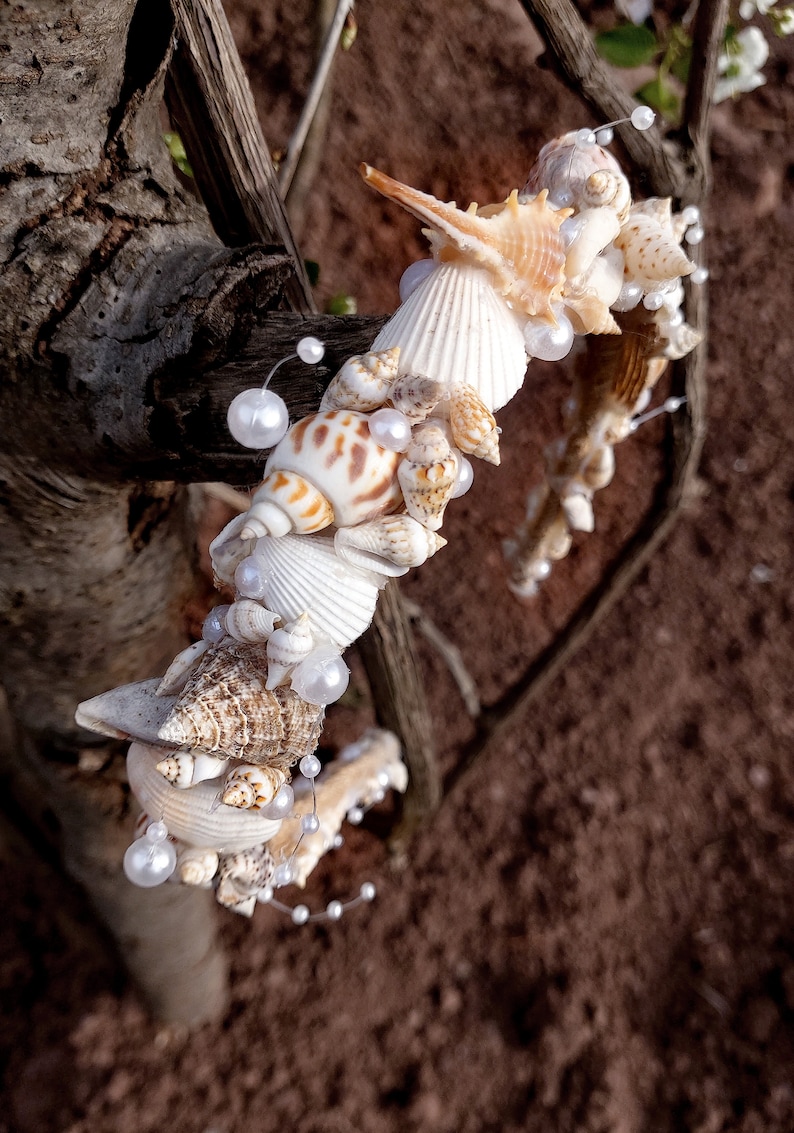May include: A collection of seashells and pearls arranged in a decorative garland, wrapped around a tree branch. The seashells are various shapes and sizes, with some having a natural brown and white pattern.