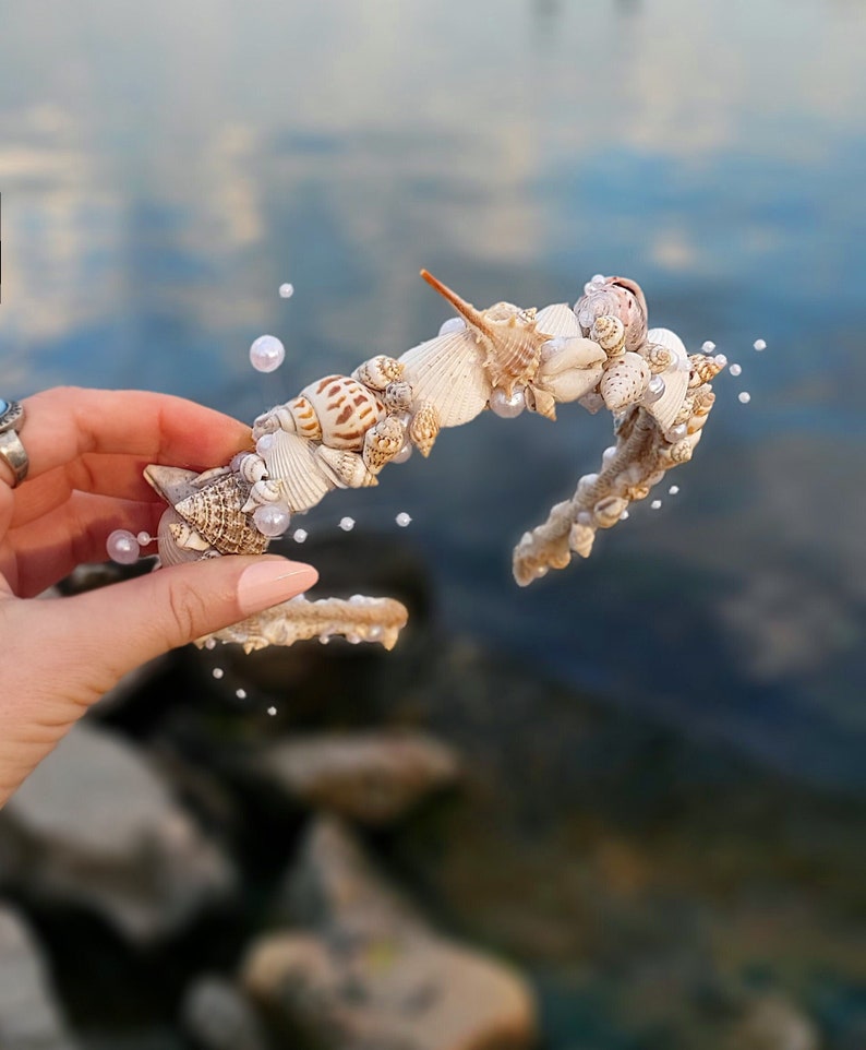 May include: A white seashell headband with white pearls. The headband is made of seashells and pearls, and is perfect for a beach wedding or a summer party.