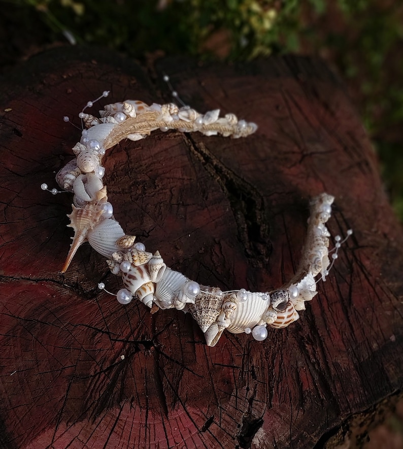 May include: A white seashell headband with pearl accents. The headband is made of natural seashells and is perfect for a beach wedding or a summer party.