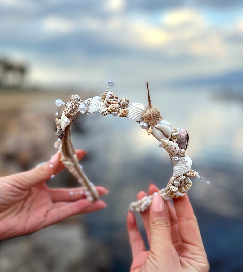 May include: A white headband decorated with seashells and pearls. The headband is made of natural materials and has a rustic look.