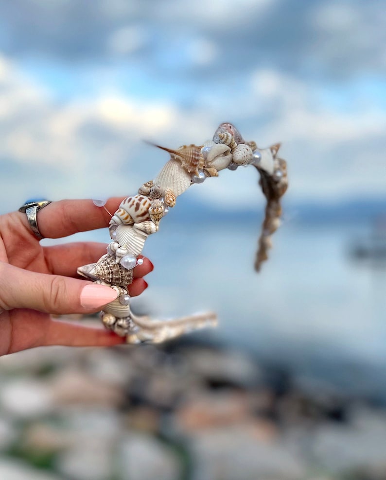 May include: A white headband decorated with seashells and pearls. The headband is a whimsical accessory for a beach-themed event.