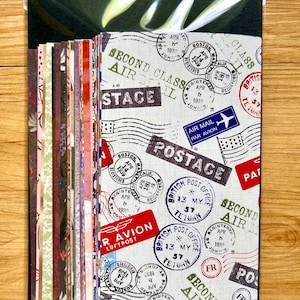 May include: A stack of rectangular paper sheets enclosed in a clear plastic sleeve. The top sheet features a vintage airmail theme with various postmarks, stamps, and text including Second Class Air Mail, Postage, and Air Mail Par Avion in red and blue.