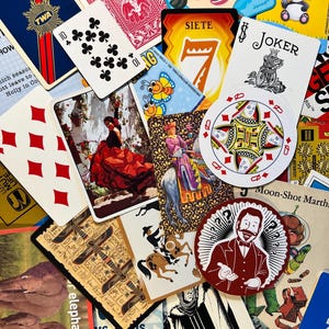 May include: A collection of playing cards, game cards, and stickers. The cards feature various designs, including suits, a joker, and illustrations. Some cards have text like "SIETE" and "RUMMY". A sticker with a man in a suit is also visible.