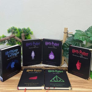 May include: A collection of six black hardcover books with gold-toned corner accents. Titles include Hermione Granger and the Call of the Phoenix, Harry Potter and the Deathly Hallows, Legion of Chaos, Methods of Rationality, Philosopher's Stone, and The Last Enemy.