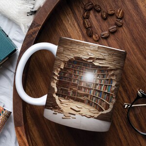 K&ouml;nnte beinhalten: Wei&szlig;e Keramiktasse mit einem Design einer Backsteinmauer mit einem Loch, das zu einer Bibliothek mit B&uuml;cherregalen f&uuml;hrt, die mit B&uuml;chern gef&uuml;llt sind. Die Bibliothek wird von einer einzigen Gl&uuml;hbirne beleuchtet.