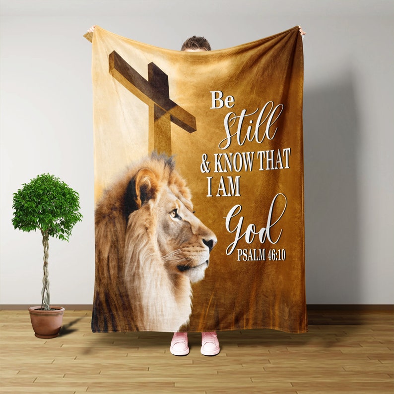 Puede incluir: Una manta de franela marr&oacute;n con la cabeza de un le&oacute;n y una cruz. La manta tiene las palabras "Be still & know that I am God Psalm 46:10" impresas en ella.