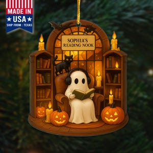 May include: A Halloween-themed ornament featuring a ghost reading in a cozy nook. The ghost wears headphones and sits in a chair, surrounded by pumpkins, candles, and a black cat. The text reads "Sophia's Reading Nook."