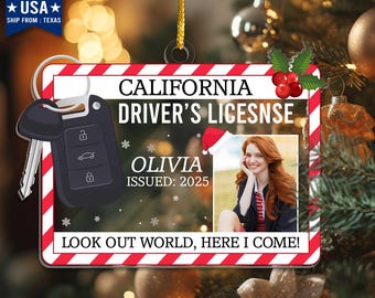 May include: A Christmas ornament shaped like a California driver's license, featuring a photo and the name "Olivia." The ornament includes a car key and the text "LOOK OUT WORLD, HERE I COME!"