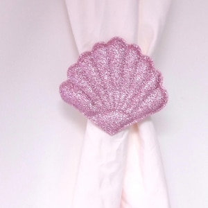 Può includere: Un fermaglio per tende a forma di conchiglia rosa scintillante. Il fermaglio è realizzato in tessuto e ha una finitura scintillante.