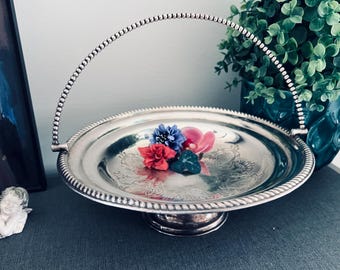 May include: A silver-colored serving tray with a beaded handle and decorative floral accents. The tray features a raised base and a detailed rim. The tray holds a small arrangement of colorful flowers.