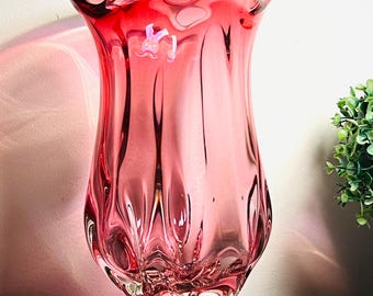 Può includere: Un alto vaso in vetro rosso traslucido con un bordo svasato e ondulato e un corpo strutturato. La base è trasparente e spessa, sostenendo il vetro rosso vibrante che si restringe leggermente verso il basso, creando una forma fluida e organica.