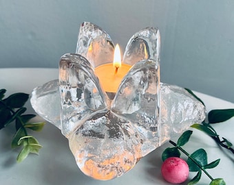 May include: A clear glass candle holder shaped like a flower with a lit tea light candle inside.